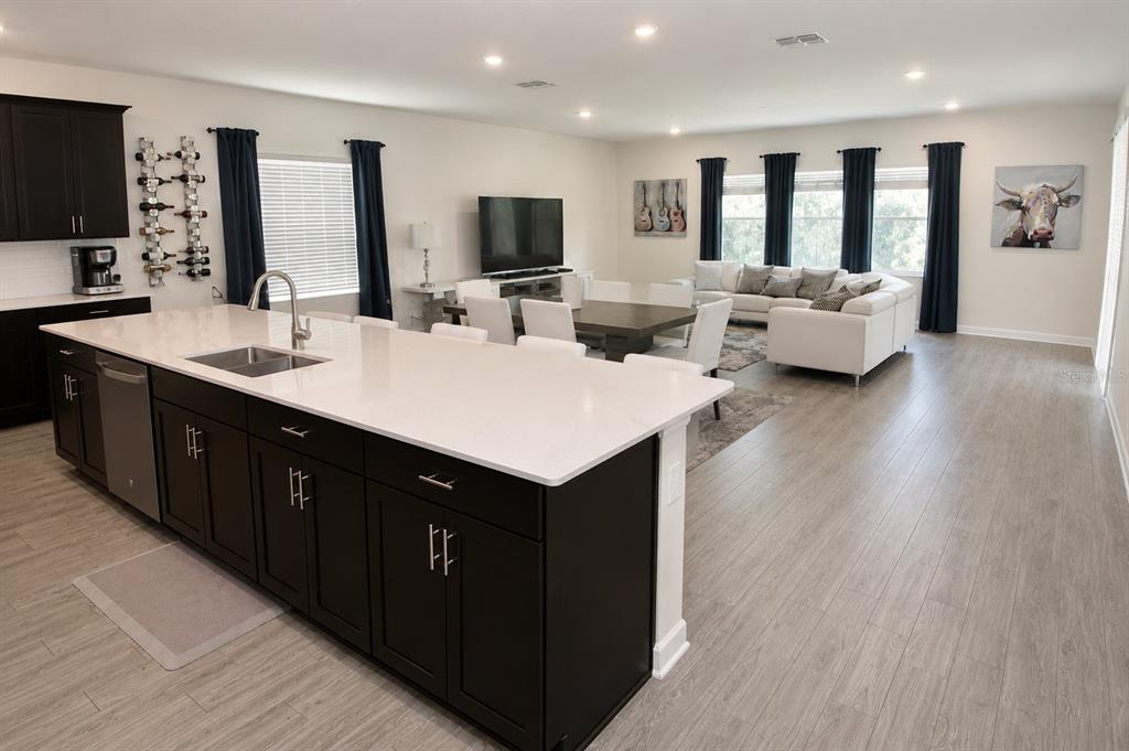 A modern open-concept kitchen with a large island overlooks a living and dining area — 11620 SATIRE STREET, ORLANDO, FL