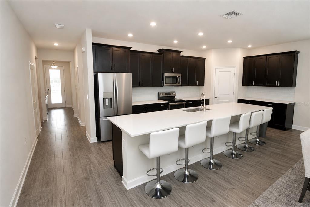 A modern kitchen features dark cabinetry, white countertops, a large island, and stainless steel appliances — 11620 SATIRE STREET, ORLANDO, FL