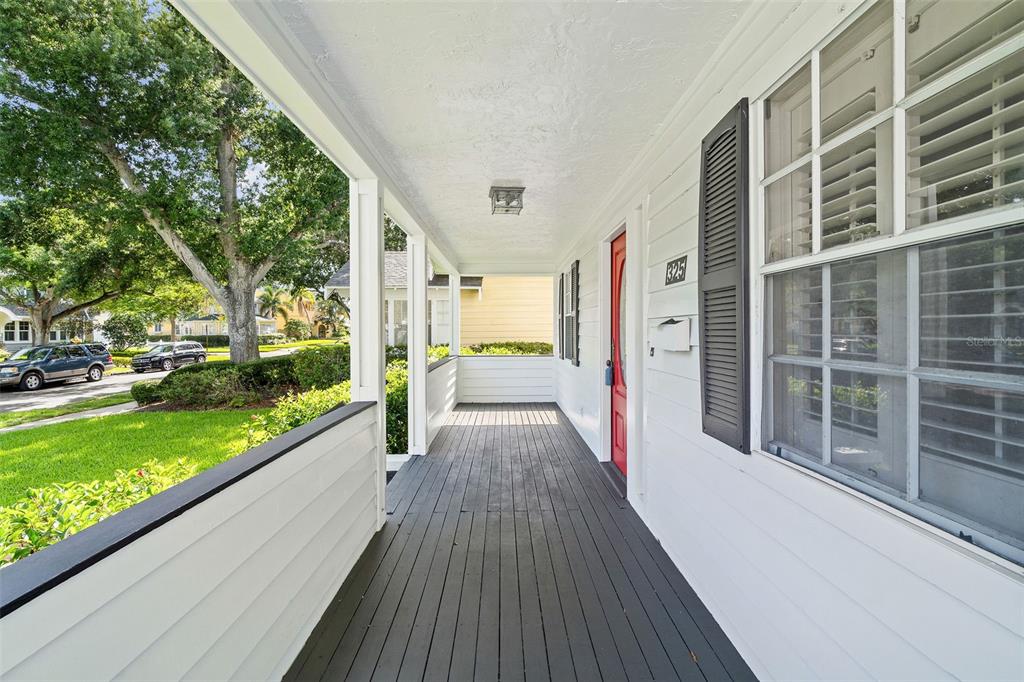 A covered front porch features dark wood decking, white siding, and a red front door — 325 17TH AVENUE NE, ST PETERSBURG, FL