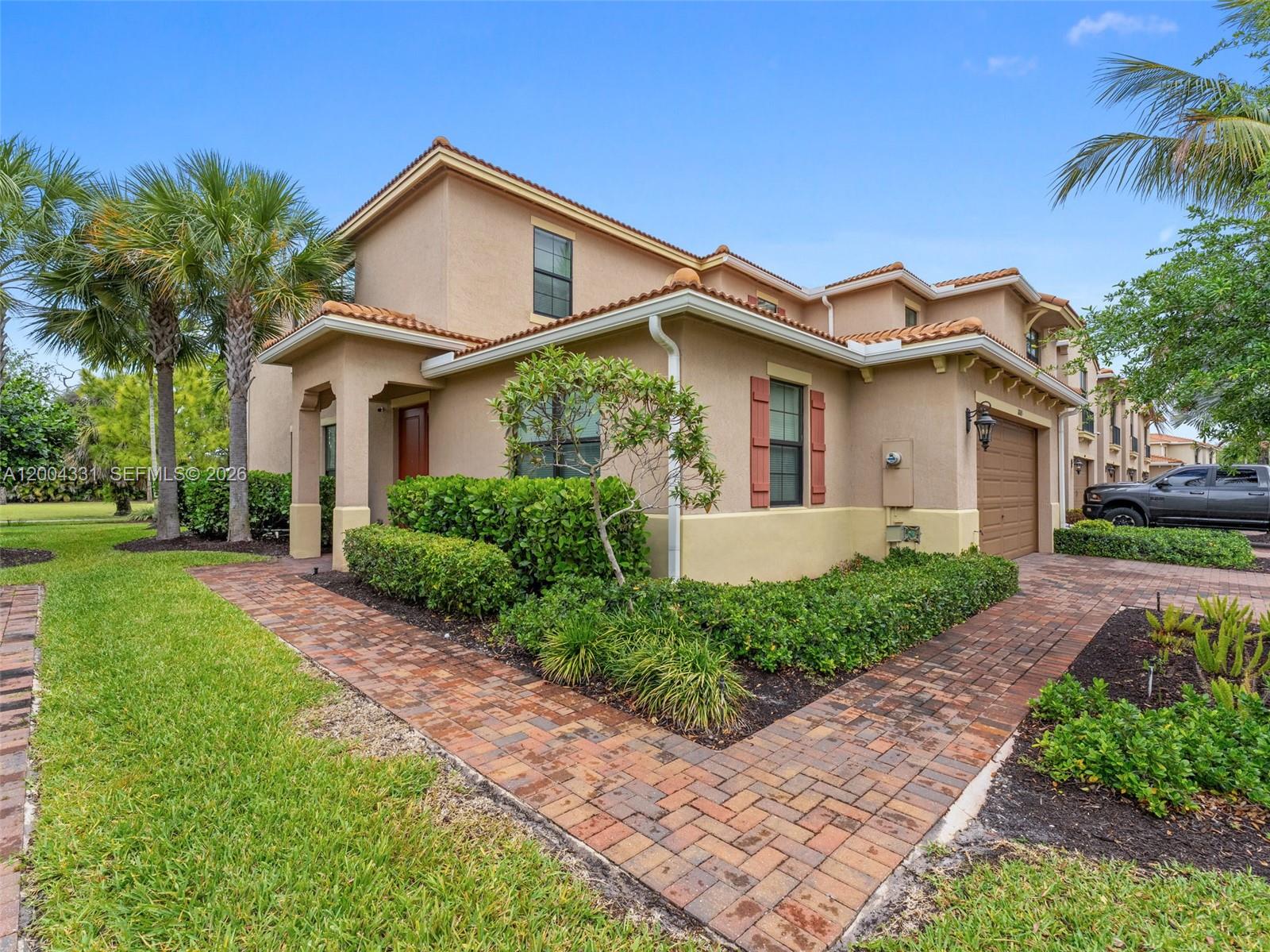 A two-story tan stucco house features a brick walkway, a garage, and palm trees — 10105 Brickhill Dr, Boca Raton FL 33428, BOCA RATON, FL