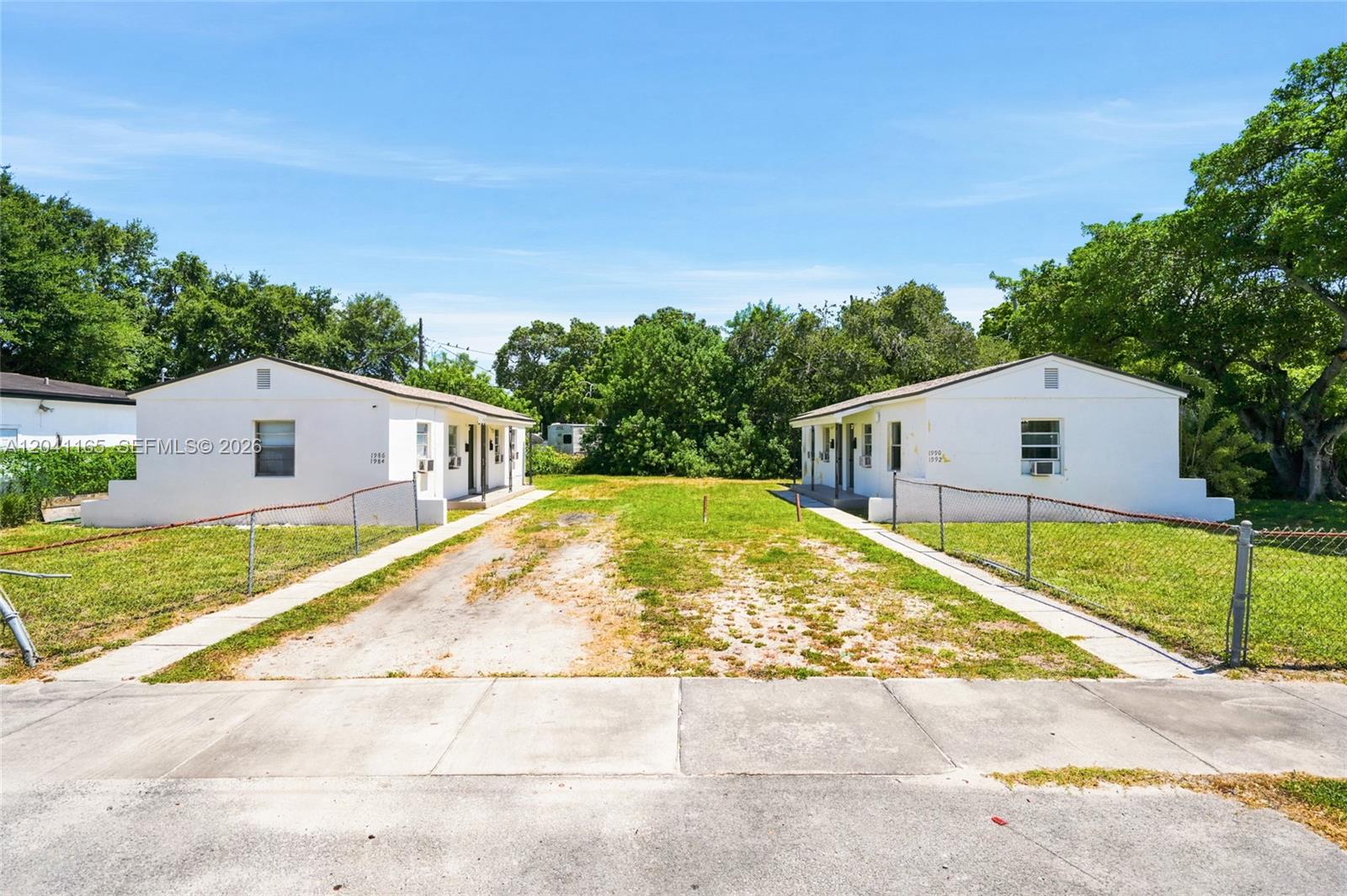 Two white single-story buildings face each other across a shared gravel and grass driveway — 1992 NW 56th St, Miami FL 33142, MIAMI, FL