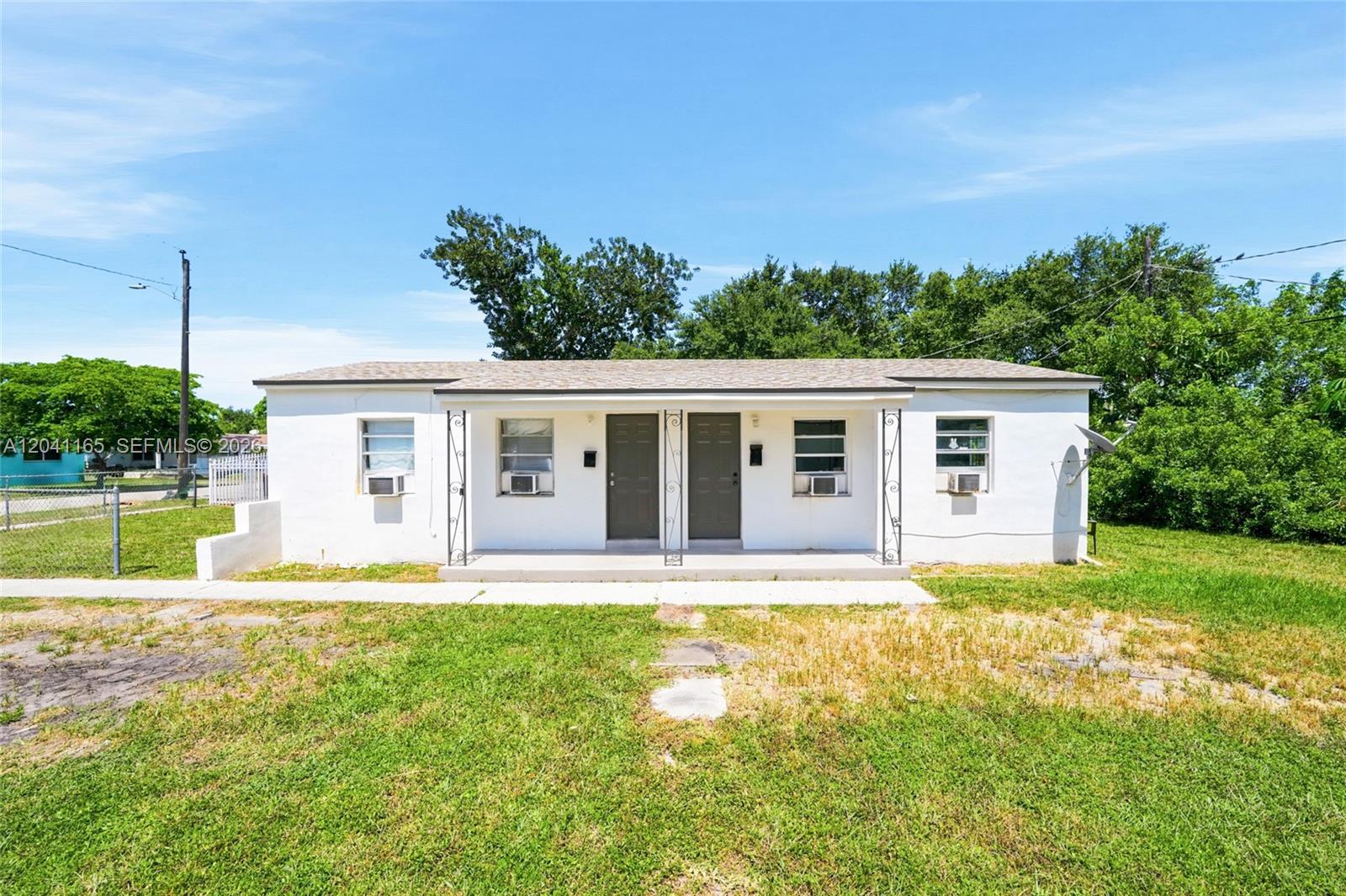 A single-story white duplex with two front doors and a covered porch under a blue sky — 1992 NW 56th St, Miami FL 33142, MIAMI, FL