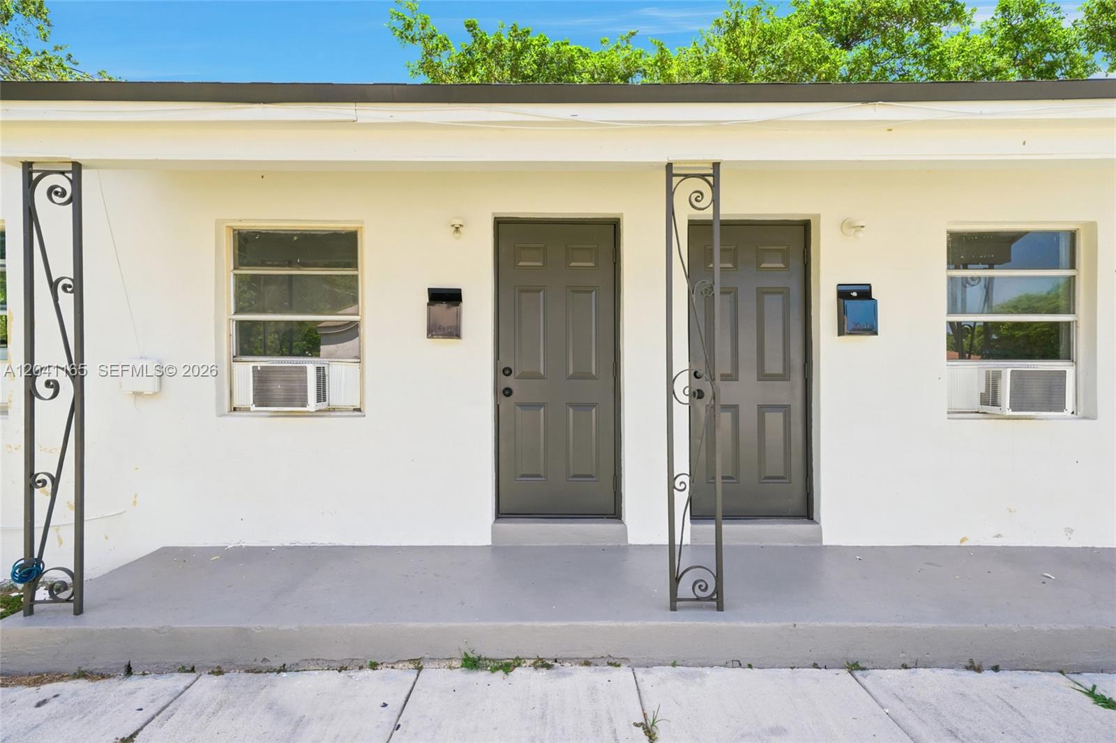 The exterior of a white building features two dark doors, windows with air conditioners, and metal columns — 1992 NW 56th St, Miami FL 33142, MIAMI, FL