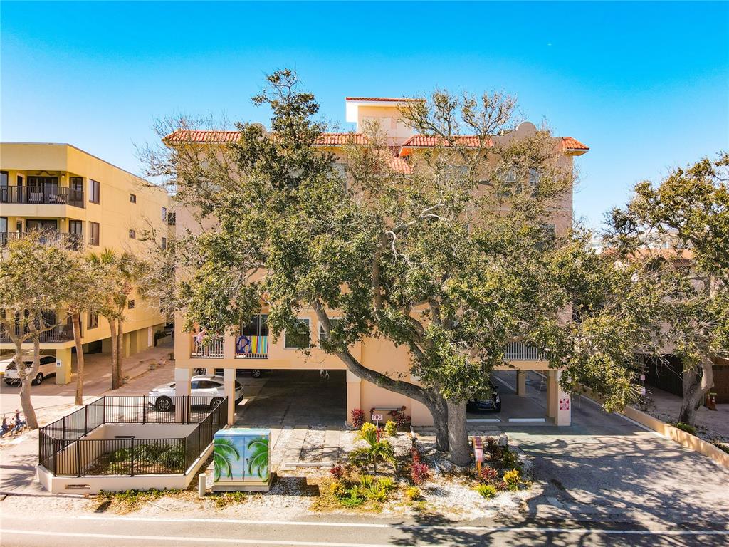 A multi-story peach-colored apartment building with covered parking and a large tree in front — 78 GULF BOULEVARD UNIT 5, INDIAN ROCKS BEACH, FL