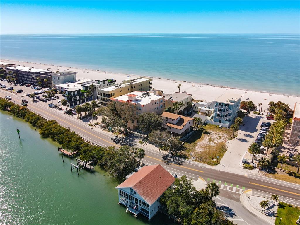 An aerial view shows a coastal road separating a bay with docks from beachfront buildings — 78 GULF BOULEVARD UNIT 5, INDIAN ROCKS BEACH, FL