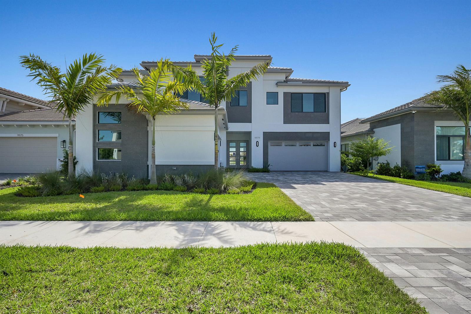 A two-story modern house with a gray and white exterior, palm trees, and paved driveway — 9979 Migration Point, Palm Beach Gardens FL 33412, PALM BEACH GARDENS, FL
