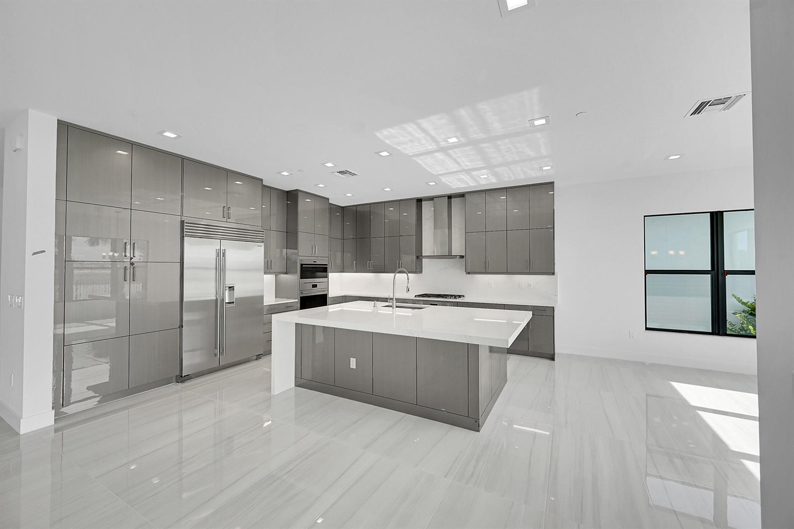 A modern kitchen features glossy gray cabinets, a large white island, and light tile flooring — 9979 Migration Point, Palm Beach Gardens FL 33412, PALM BEACH GARDENS, FL