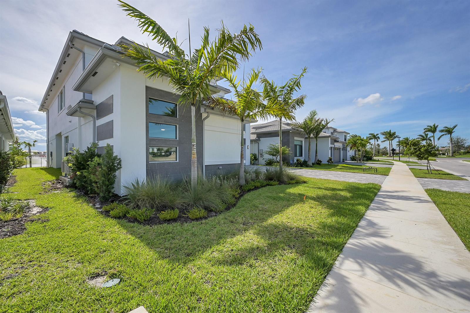 A modern two-story house with a white and gray exterior sits beside a paved sidewalk — 9979 Migration Point, Palm Beach Gardens FL 33412, PALM BEACH GARDENS, FL