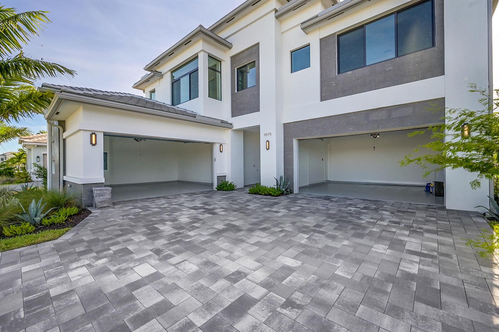 A two-story house exterior features a paved driveway, two open garages, and modern architectural details — 9979 Migration Point, Palm Beach Gardens FL 33412, PALM BEACH GARDENS, FL