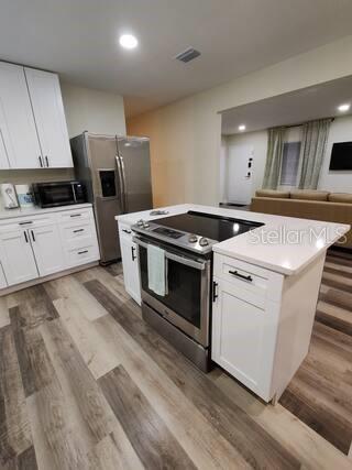 A kitchen features white cabinets, stainless steel appliances, a center island, and wood-look flooring — 5810 N 19TH STREET, TAMPA, FL