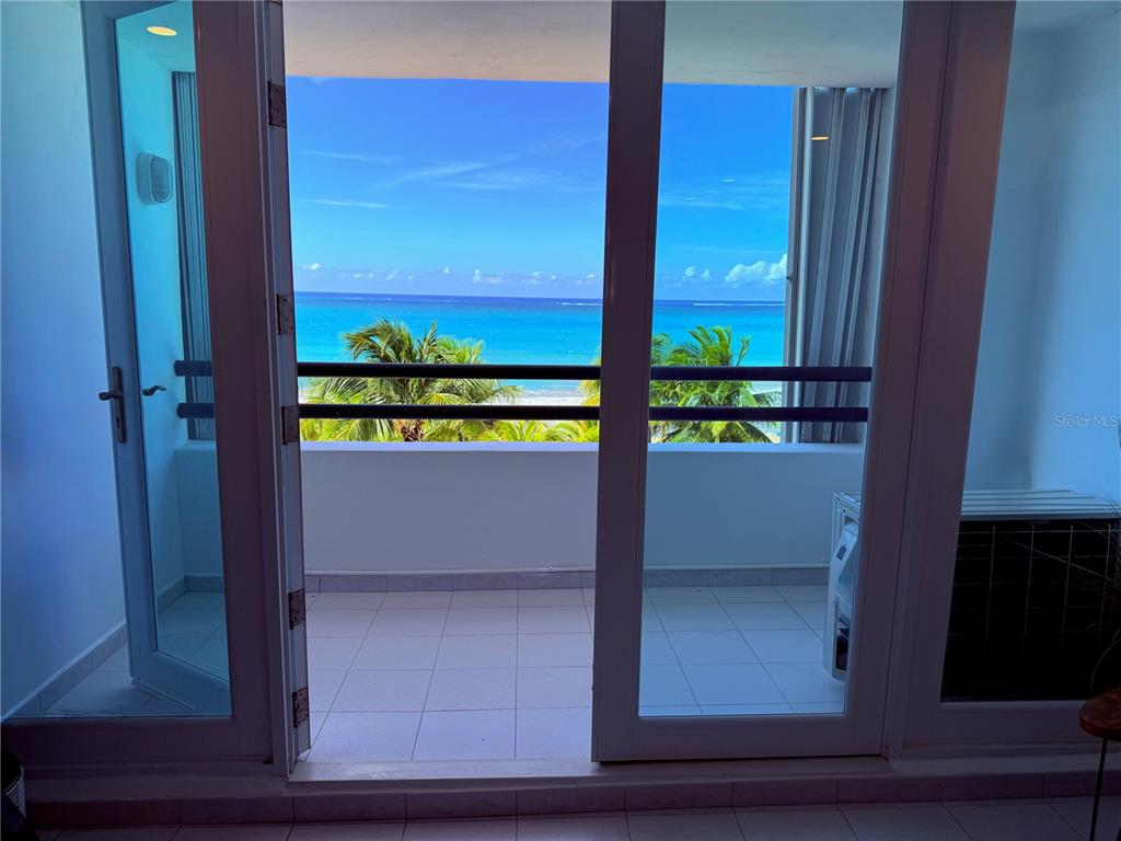 A view from an indoor room through glass doors onto a balcony overlooking the ocean — 1 HORIZONTE UNIT 514, CAROLINA, PR