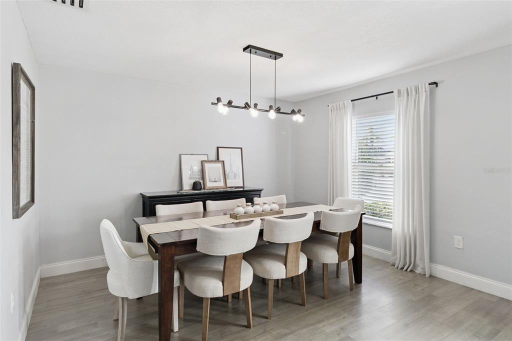 A dining room features a dark wood table, six upholstered chairs, and a modern light fixture — 4981 SPINET DRIVE, MELBOURNE, FL