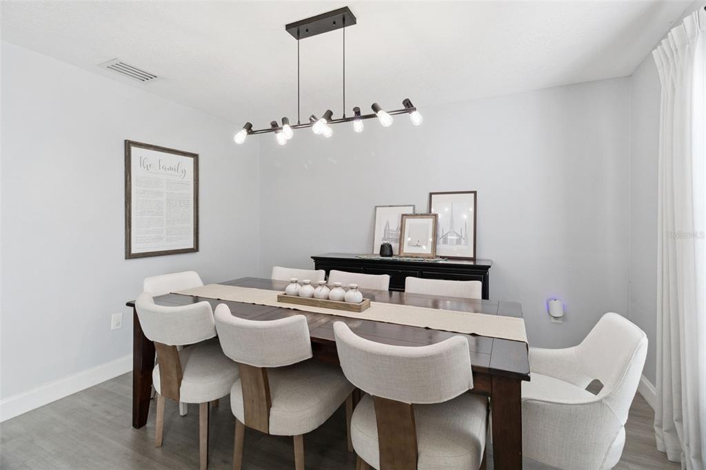 A dining room features a dark wood table, upholstered chairs, and a modern linear chandelier — 4981 SPINET DRIVE, MELBOURNE, FL