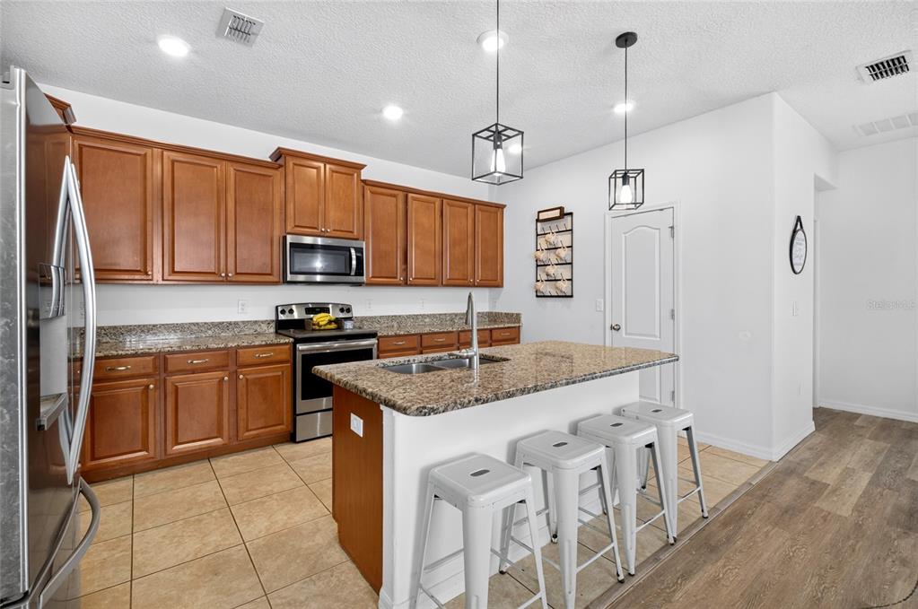 A kitchen features wood cabinets, granite countertops, a center island with stools, and stainless appliances — 4841 HAVILLAND DRIVE, MOUNT DORA, FL