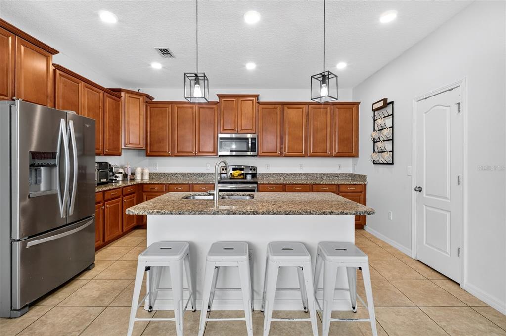 A kitchen features wood cabinets, granite countertops, a central island with stools, and stainless appliances — 4841 HAVILLAND DRIVE, MOUNT DORA, FL