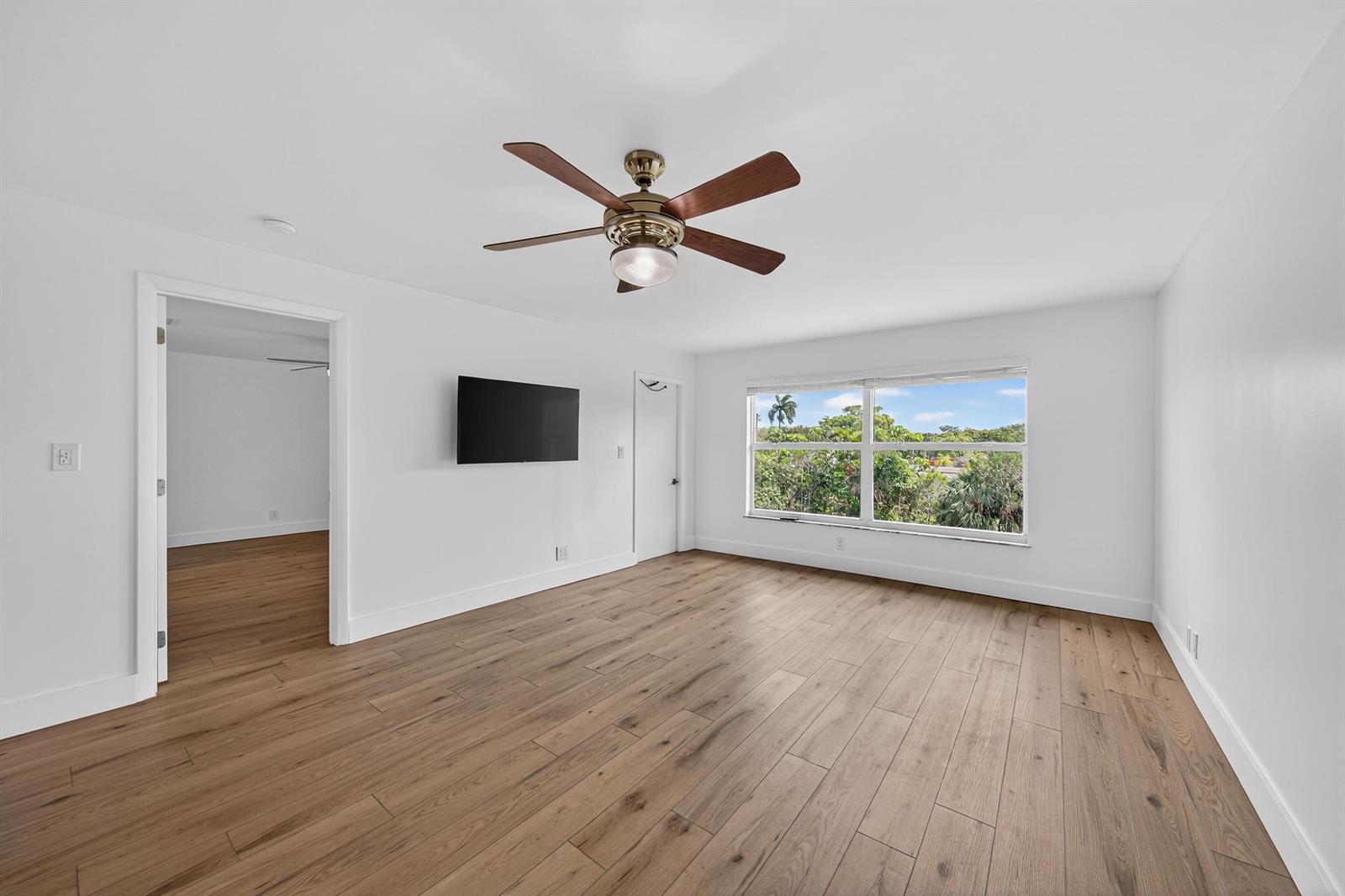 A bedroom with white walls, wood-look flooring, a ceiling fan, and a wall-mounted television — 6570 Royal Palm Boulevard # 306j, Margate FL 33063, MARGATE, FL