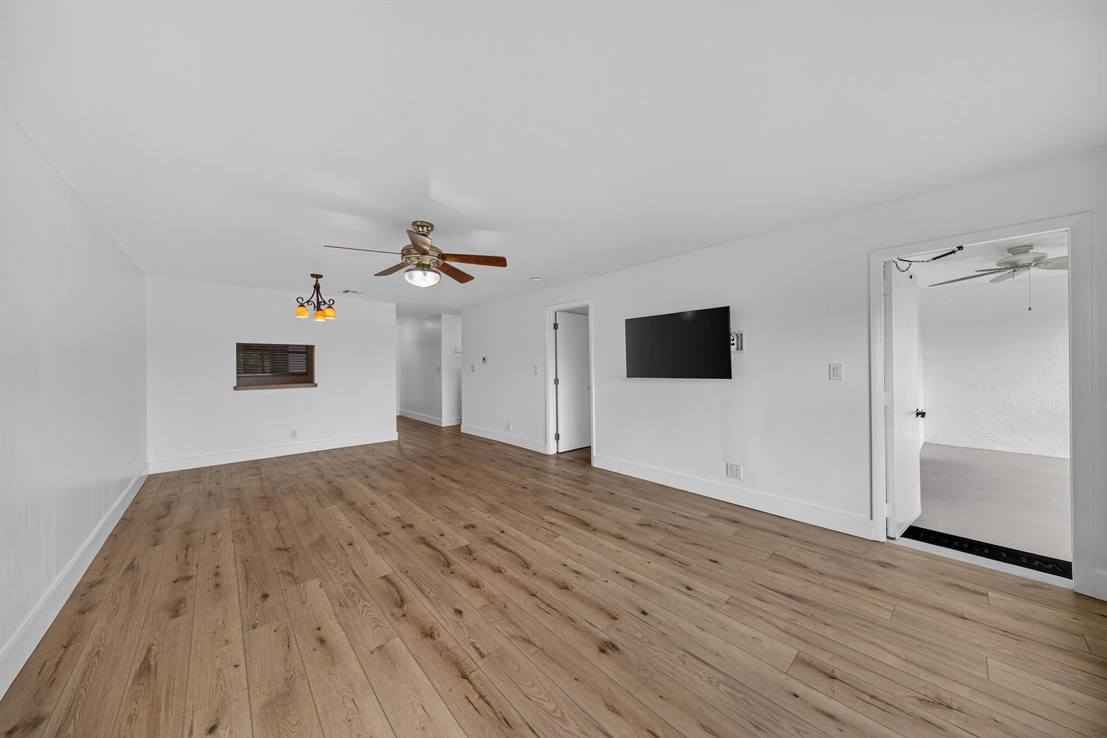 A living room with white walls, wood-look flooring, a ceiling fan, and a wall-mounted television — 6570 Royal Palm Boulevard # 306j, Margate FL 33063, MARGATE, FL