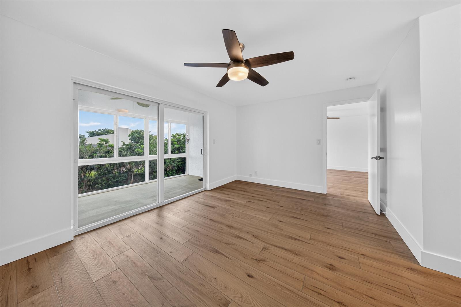 A bright, empty bedroom features wood-look flooring, a ceiling fan, and sliding glass doors — 6570 Royal Palm Boulevard # 306j, Margate FL 33063, MARGATE, FL