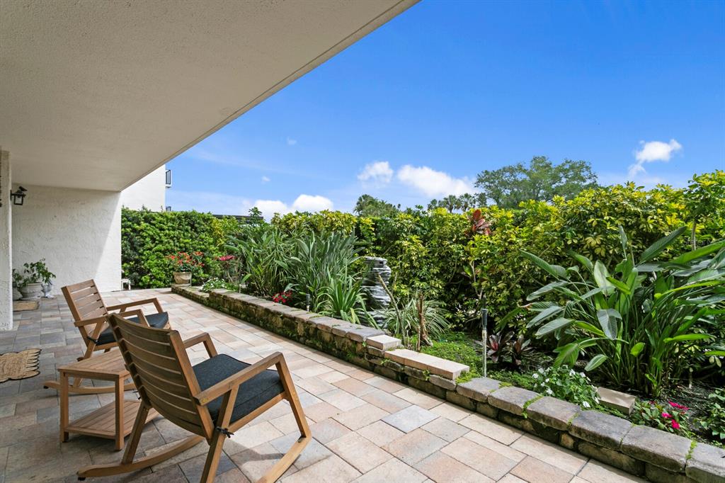 A paved patio features two wooden rocking chairs and a stone-bordered garden under a roof — 100 OAKMONT LANE UNIT 105, BELLEAIR, FL