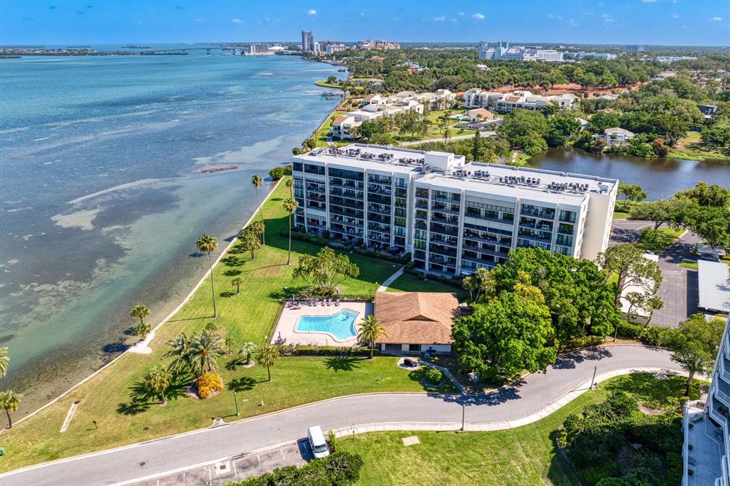 An aerial view shows a multi-story apartment building next to a pool and the water — 100 OAKMONT LANE UNIT 105, BELLEAIR, FL