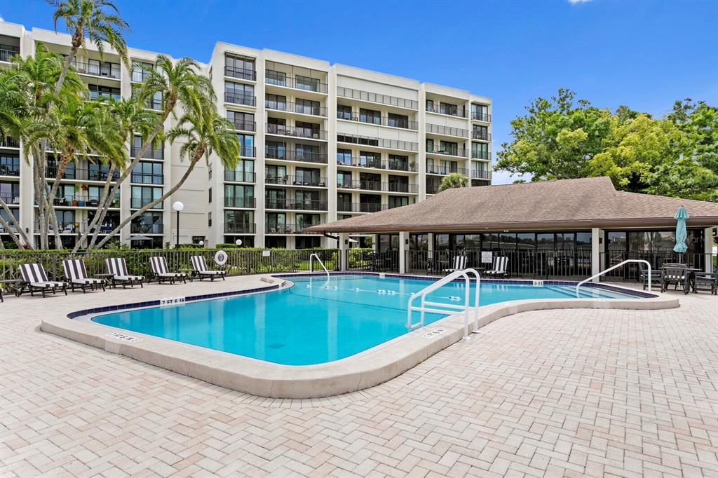An outdoor swimming pool with a paved deck and a multi-story apartment building in background — 100 OAKMONT LANE UNIT 105, BELLEAIR, FL