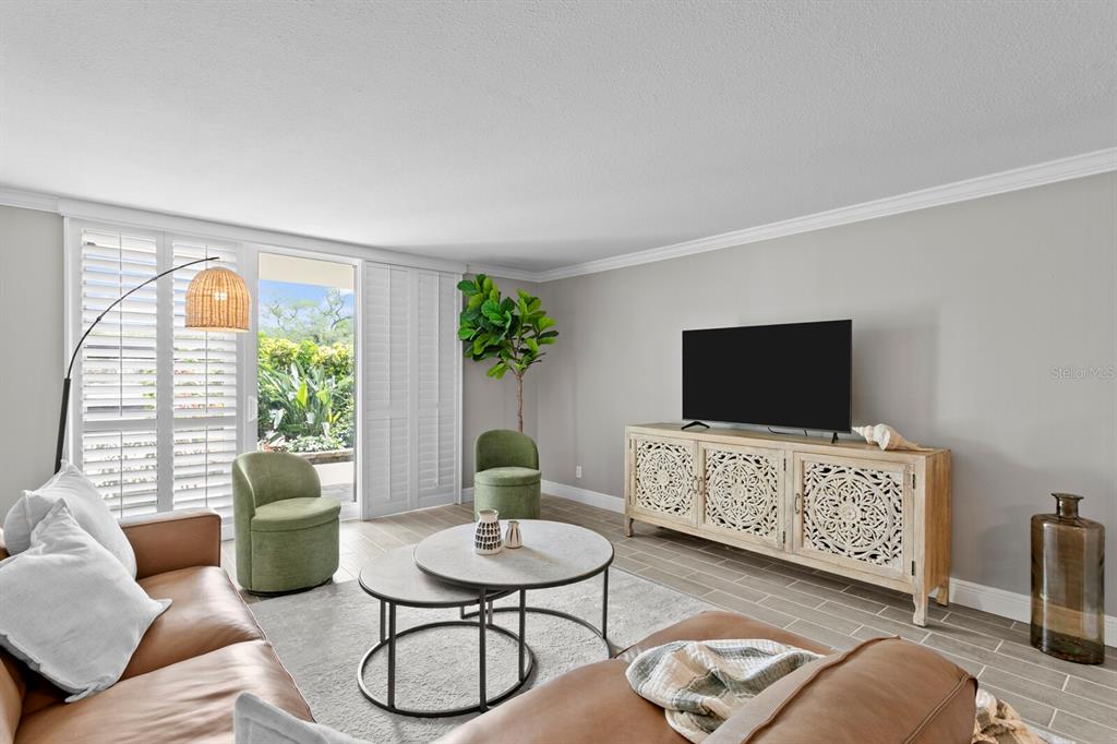 A living room features a leather sofa, two green chairs, nesting tables, and a television console — 100 OAKMONT LANE UNIT 105, BELLEAIR, FL