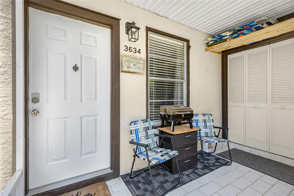 A covered patio features a white front door, two folding chairs, and a small grill — 3634 59TH AVENUE W, BRADENTON, FL