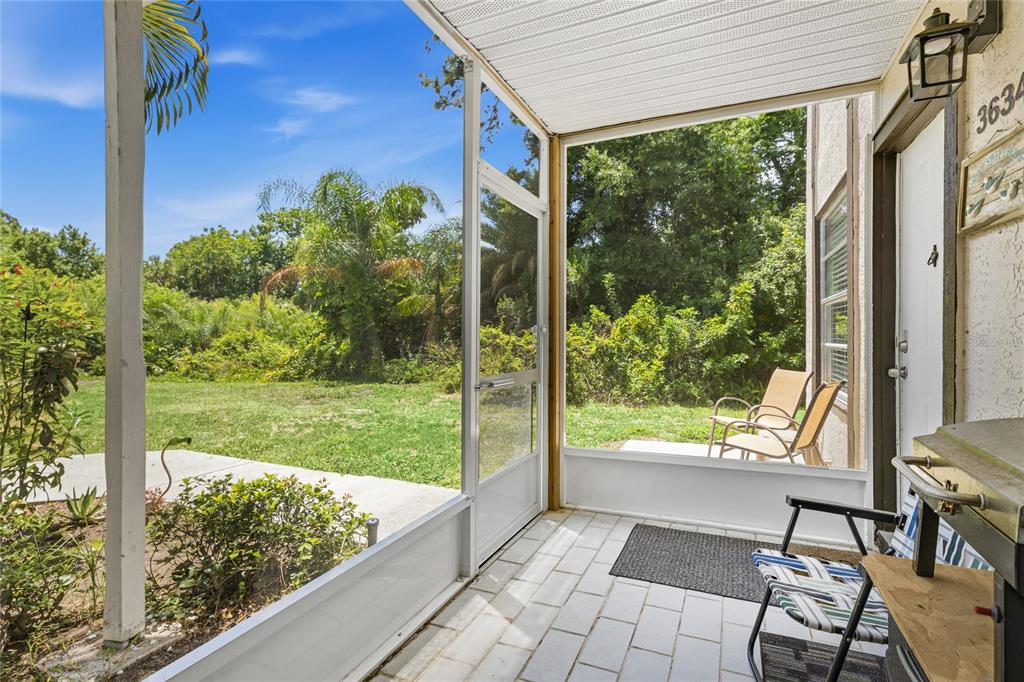 A screened-in patio with tiled flooring overlooks a grassy yard and dense green trees — 3634 59TH AVENUE W, BRADENTON, FL