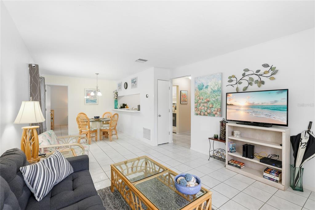 A living room with white tile floors, a grey sofa, and a dining area beyond — 3634 59TH AVENUE W, BRADENTON, FL