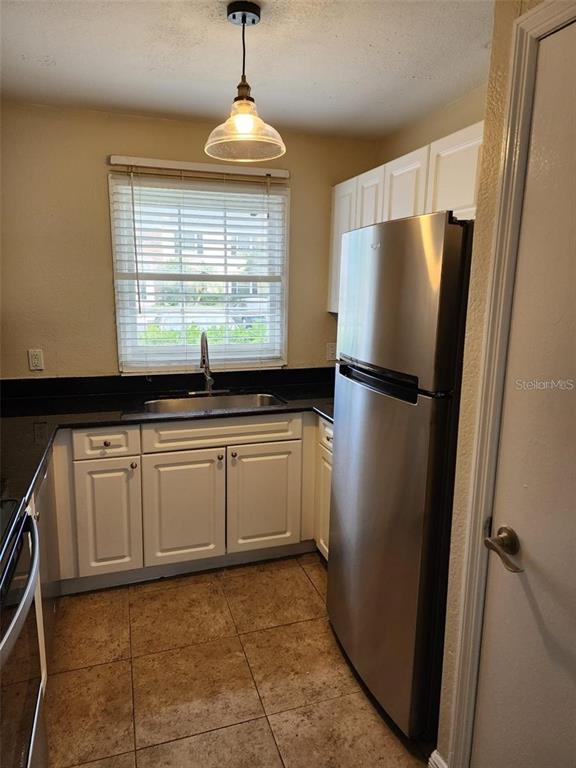 A kitchen features white cabinets, a stainless steel refrigerator, a sink, and tile flooring — 13698 ORANGE SUNSET DRIVE, TAMPA, FL