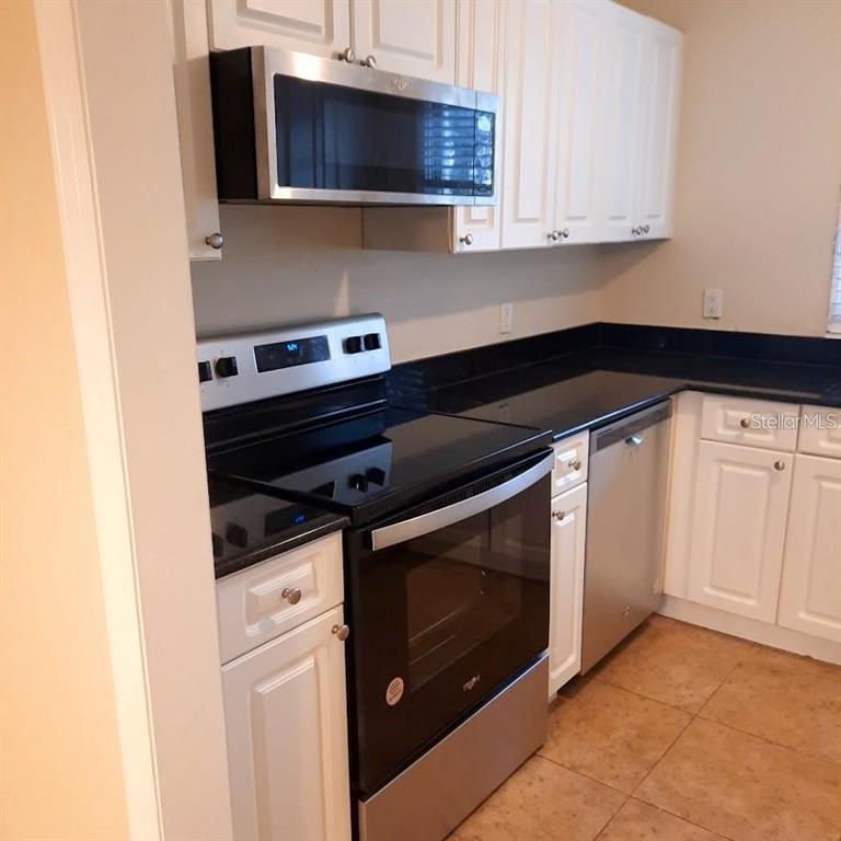 A kitchen features white cabinets, stainless steel appliances, and black countertops over tile flooring — 13698 ORANGE SUNSET DRIVE, TAMPA, FL