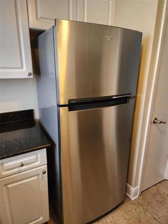 A stainless steel top-freezer refrigerator stands in a kitchen with white cabinets and dark countertops — 13698 ORANGE SUNSET DRIVE, TAMPA, FL