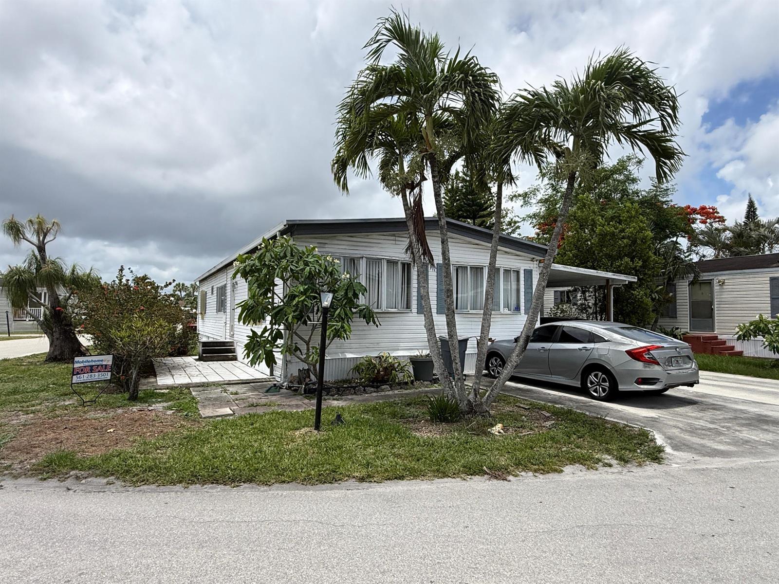 A white mobile home with a silver sedan parked in the driveway under palm trees — 4707 Nancy Drive # 757, FL 33463, FL