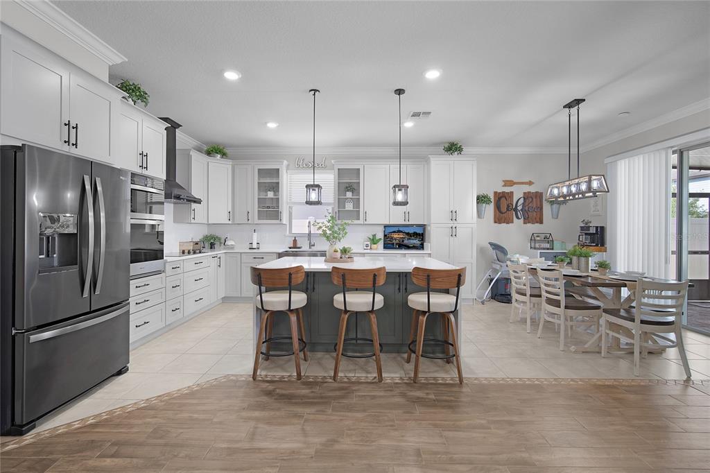 A bright kitchen features white cabinetry, a dark gray island with barstools, and tile flooring — 1796 CAYMAN COVE CIRCLE, ST CLOUD, FL