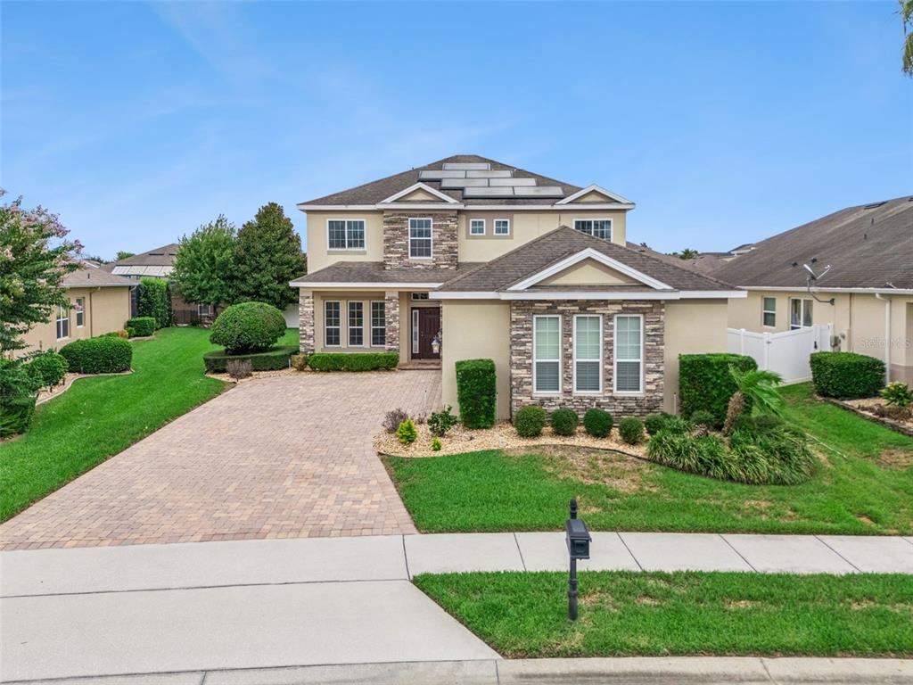 A two-story suburban house features a stone facade, a paved driveway, and rooftop solar panels — 2045 SANDY GARDEN LANE, WINTER GARDEN, FL