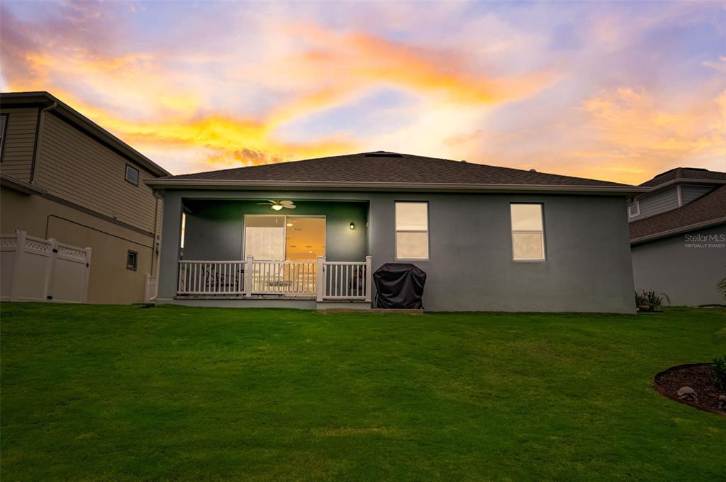 The rear exterior of a house features a covered patio, a lawn, and a sunset — 5413 WISHING ARCH DRIVE, APOLLO BEACH, FL