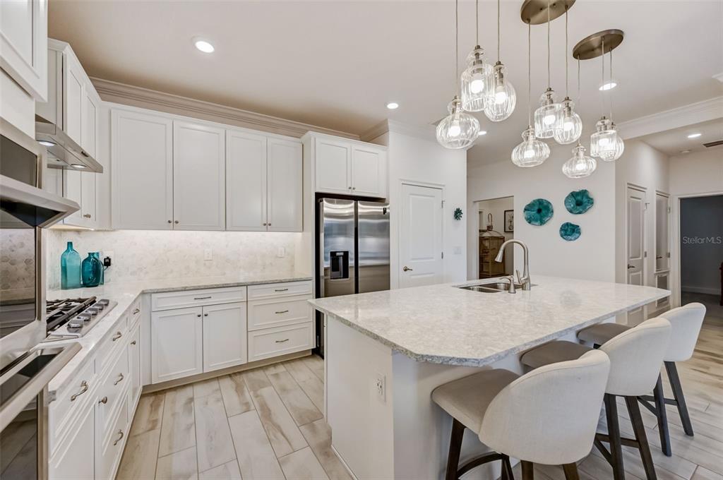 A modern kitchen features white cabinetry, a large island with bar seating, and pendant lighting — 5413 WISHING ARCH DRIVE, APOLLO BEACH, FL