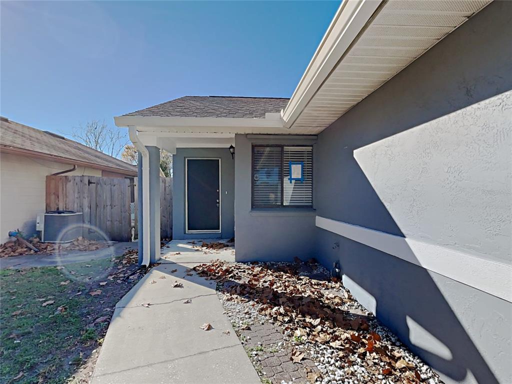 A gray exterior wall with a front door, a window, and a concrete walkway — 11532 BENBOW COURT, ORLANDO, FL
