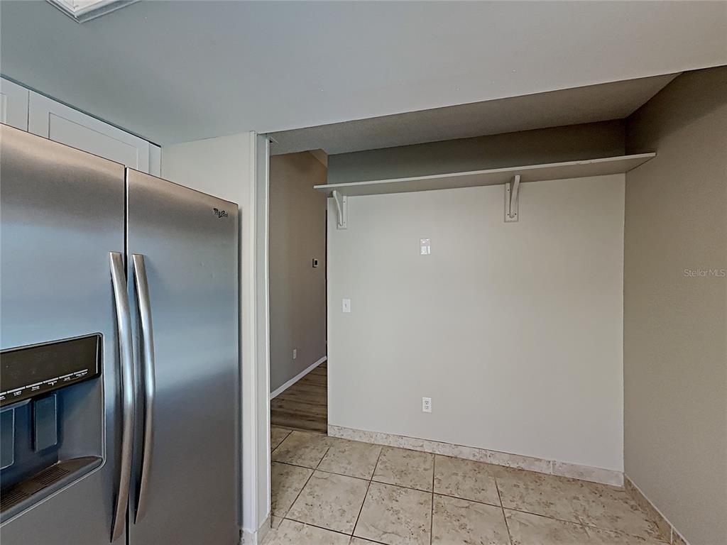 A stainless steel refrigerator stands beside a tiled kitchen area with a wall-mounted shelf — 11532 BENBOW COURT, ORLANDO, FL