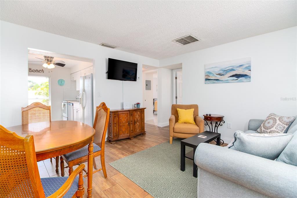 A living room and dining area feature wood-look flooring, a television, and neutral walls — 7209 COQUINA WAY UNIT 4, ST PETE BEACH, FL