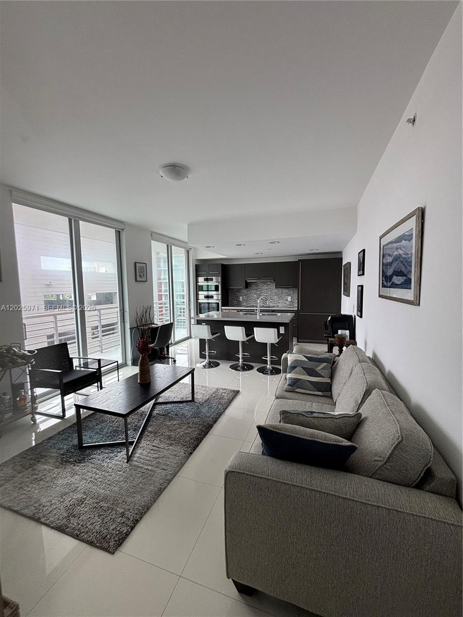 A modern open-concept living room features a gray sofa, coffee table, and an adjacent kitchen — 7875 NW 107th Ave # 504, Doral FL 33178, DORAL, FL