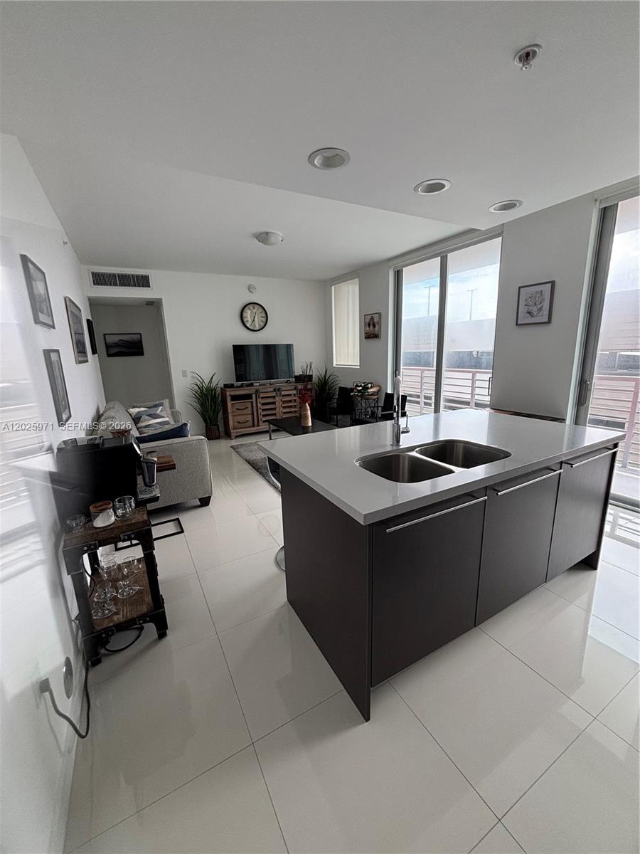 A modern kitchen island with a double sink overlooks a living area with tile flooring — 7875 NW 107th Ave # 504, Doral FL 33178, DORAL, FL