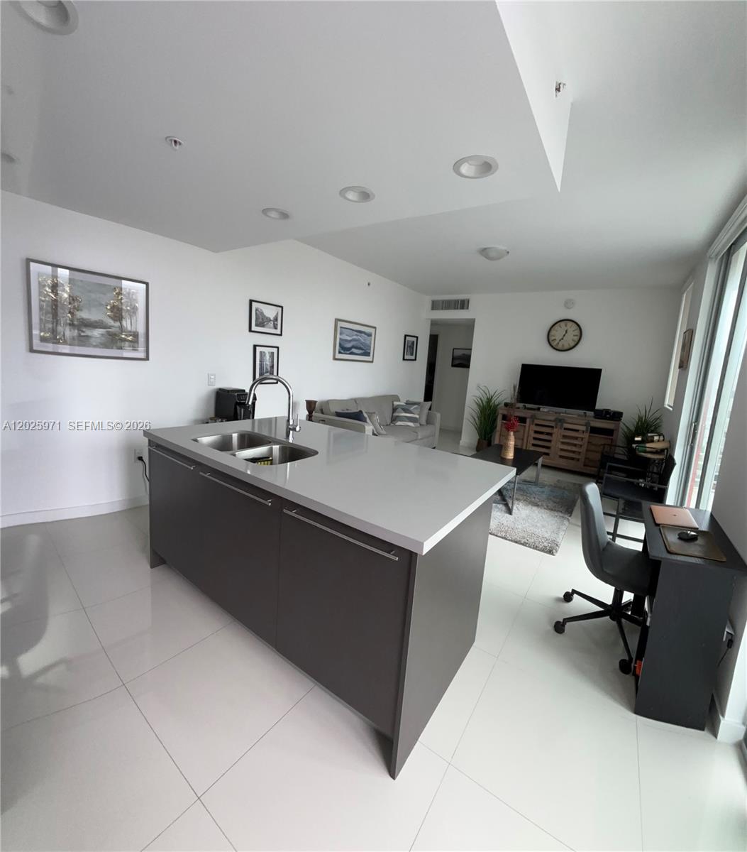 A modern kitchen island with a gray base and white countertop sits in an open-concept room — 7875 NW 107th Ave # 504, Doral FL 33178, DORAL, FL