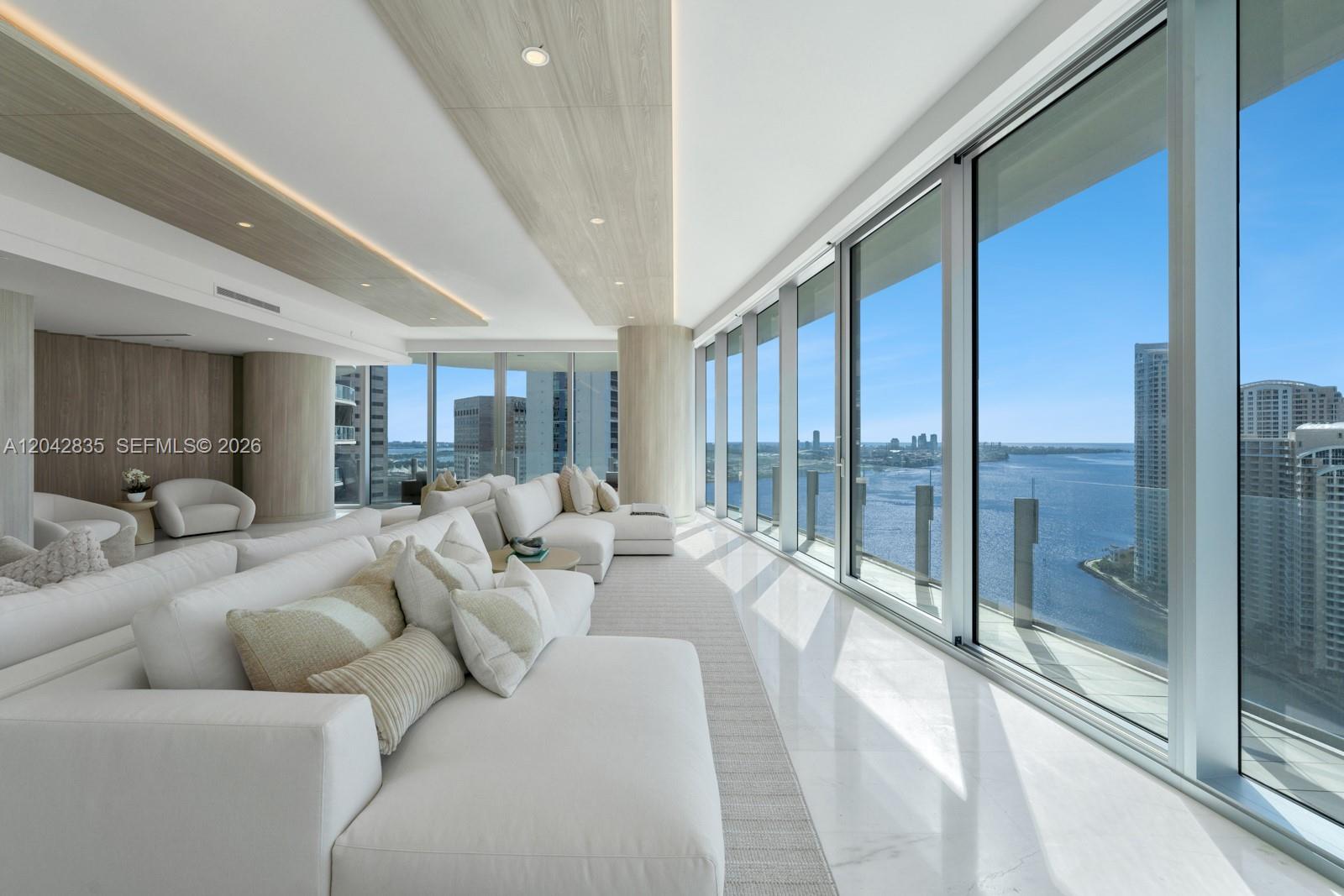 A bright living room features white sectionals, marble floors, and floor-to-ceiling windows overlooking the water — 300 Biscayne Boulevard Way # 2701, Miami FL 33131, MIAMI, FL