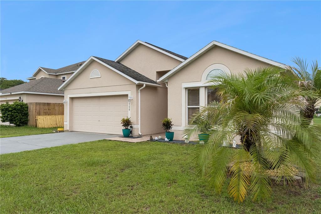 A single-story tan house with a two-car garage and a palm tree in the front yard — 10354 LAXTON STREET, ORLANDO, FL