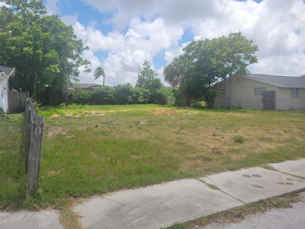 A vacant, grassy residential lot sits between two existing houses under a cloudy sky — 7404 INGLESIDE DRIVE, PORT RICHEY, FL