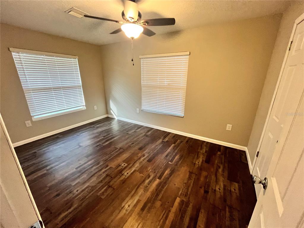 An empty bedroom features dark wood-look flooring, two windows with blinds, and a ceiling fan — 601 ANDYS COURT, ORANGE CITY, FL