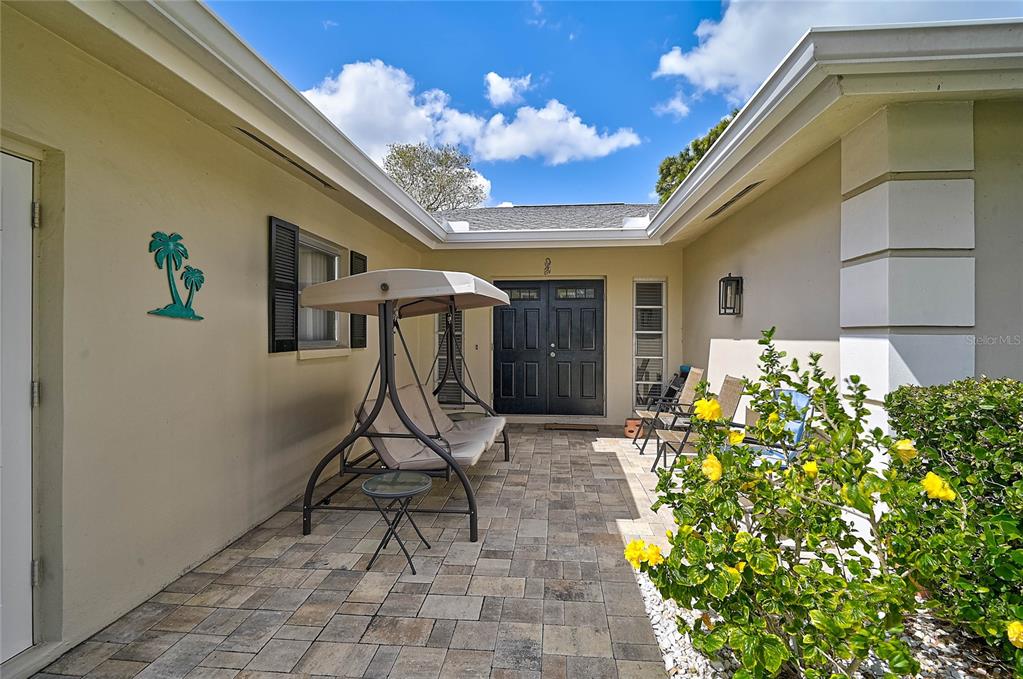 A paved courtyard leads to a dark double-door entrance with a swing and landscaping — 7128 W COUNTRY CLUB DRIVE N, SARASOTA, FL