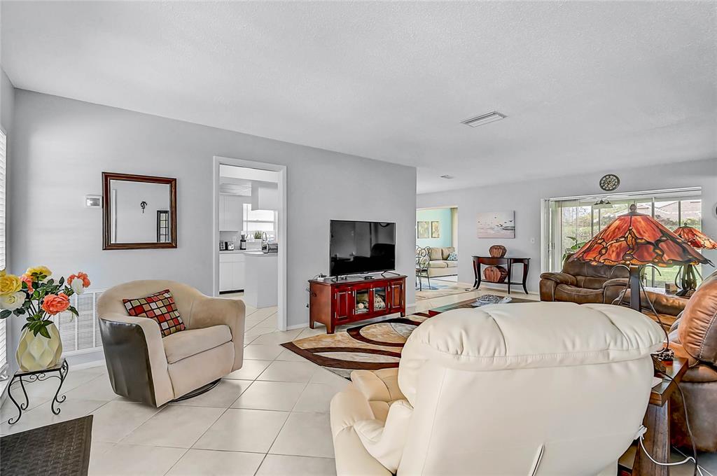A living room features light gray walls, tile flooring, a television, and several armchairs — 7128 W COUNTRY CLUB DRIVE N, SARASOTA, FL