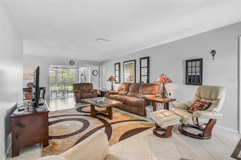 A living room features tile flooring, a brown sofa, a recliner, and a sliding glass door — 7128 W COUNTRY CLUB DRIVE N, SARASOTA, FL